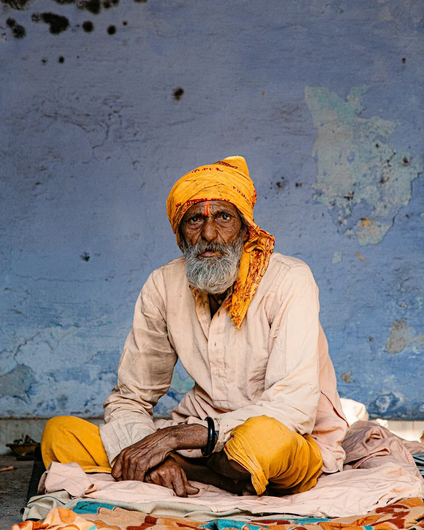 Man in an orange turban sitting against a blue wall