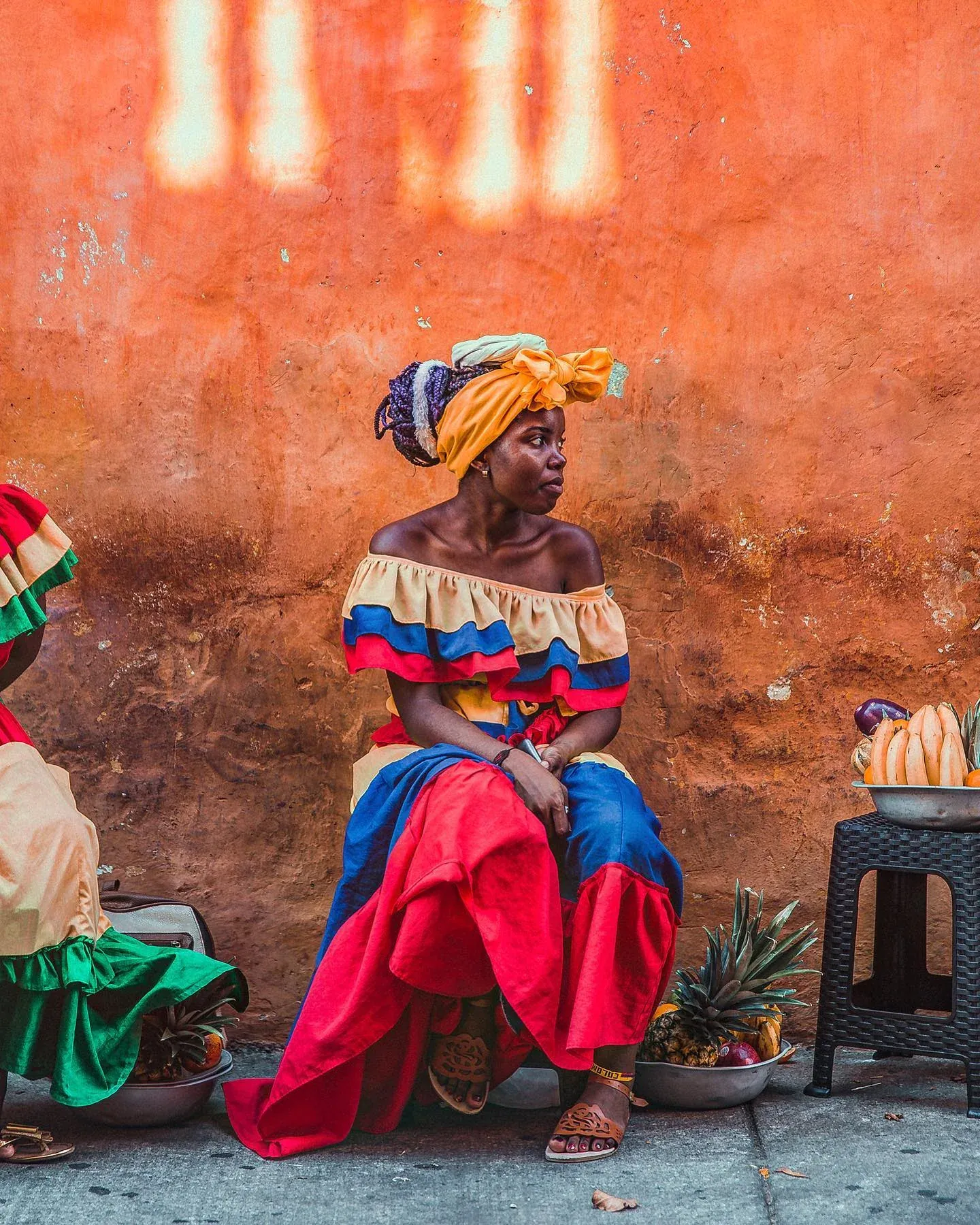 Fruit seller in a bright dress against an orange wall
