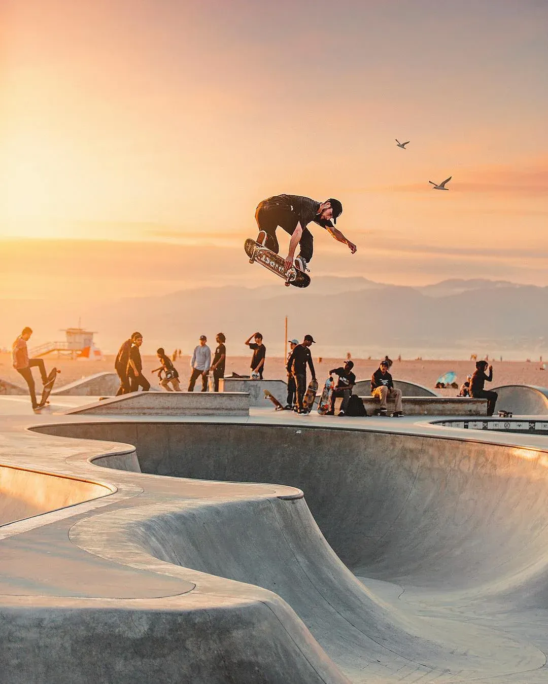 Skater in the air above a beach skatepark at sunset