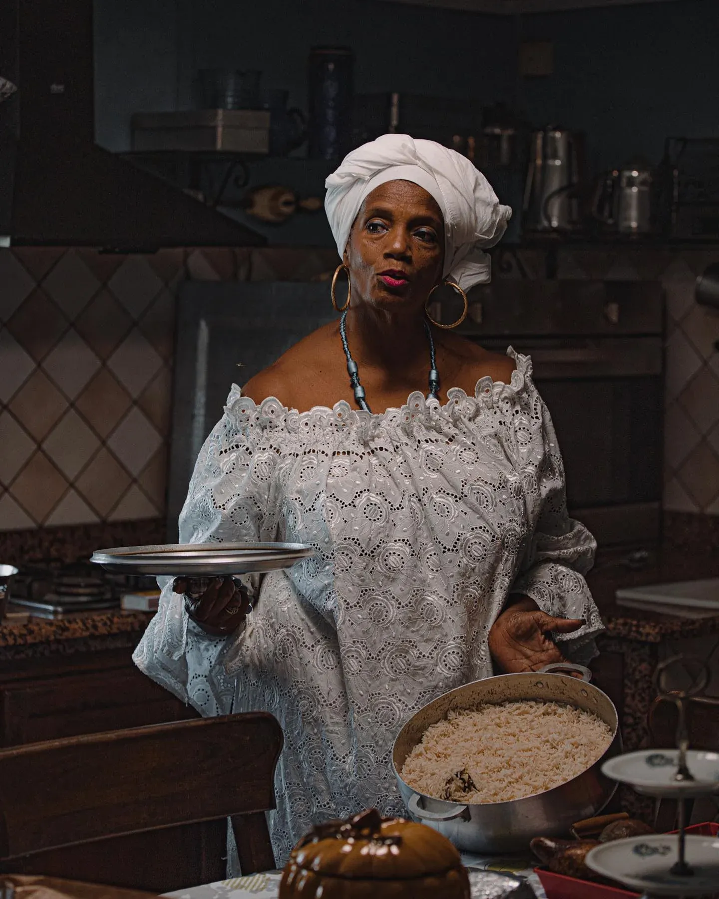 Cook in a white headwrap holding a pan of rice