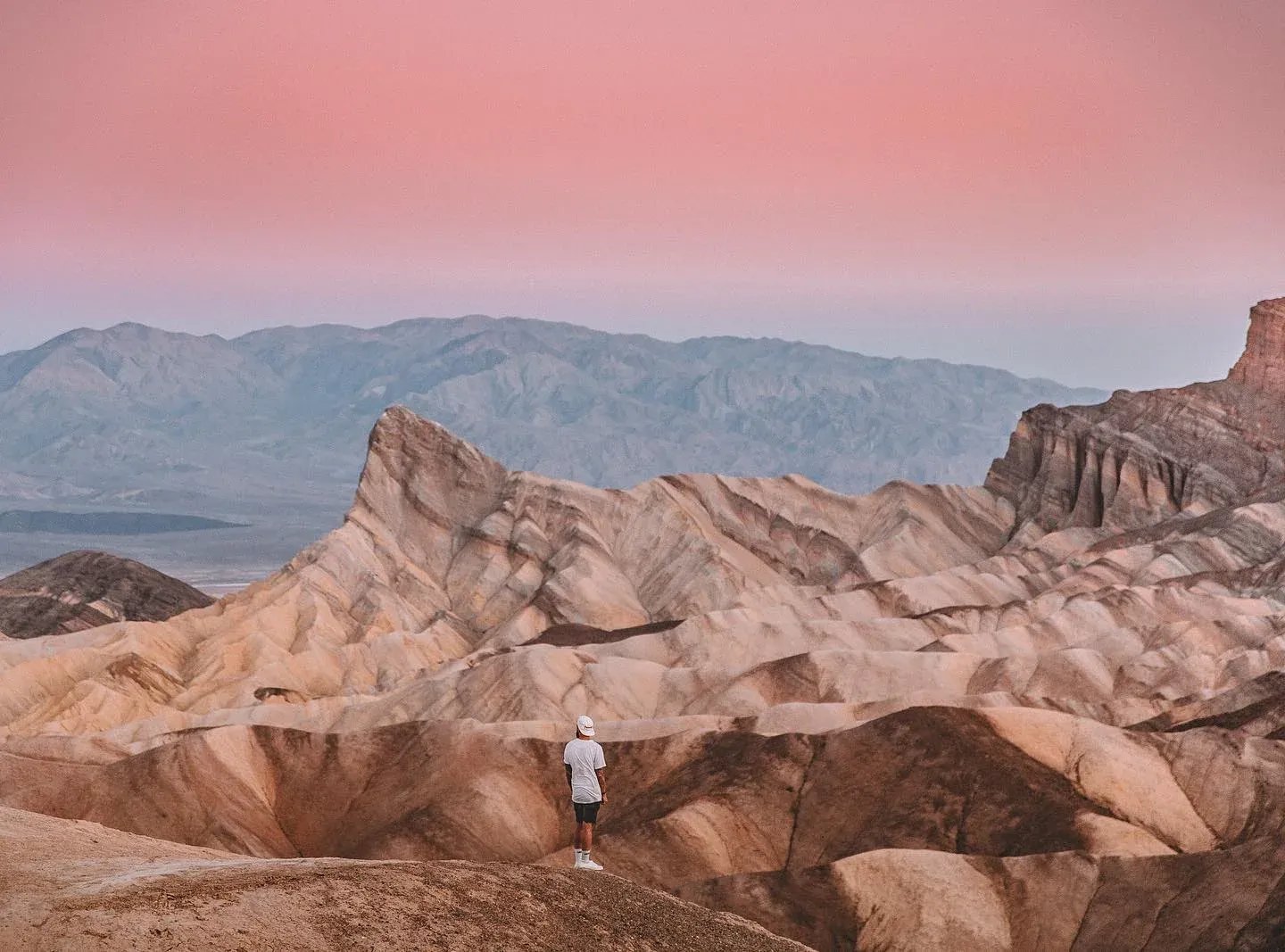 Badlands under a pink sky with a lone figure