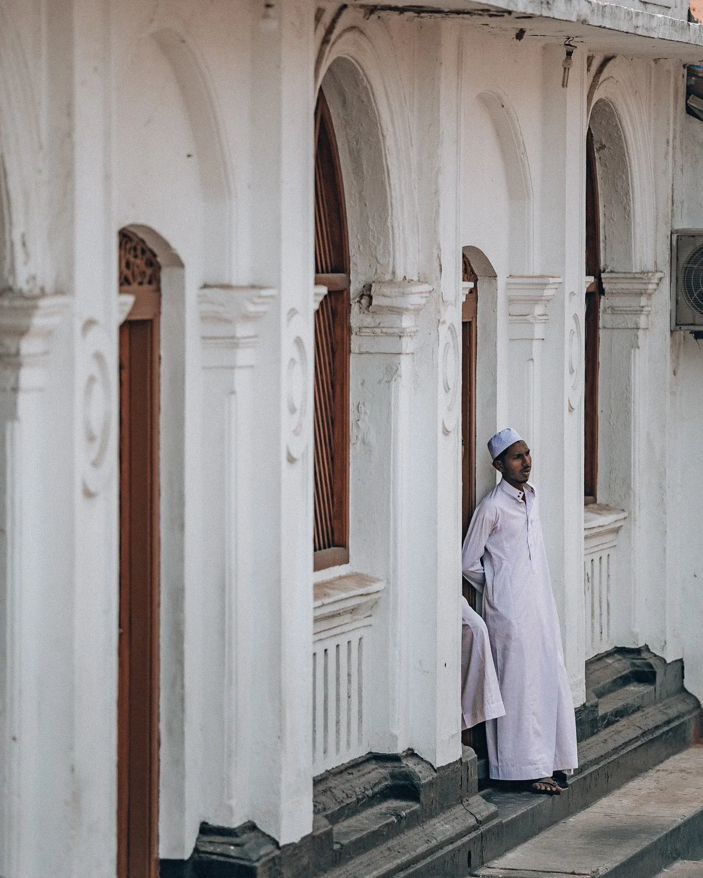 Man in a white robe leaning in an arched doorway